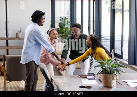 Diverse team collaborating in modern office, joining hands in teamwork celebration Stock Photo