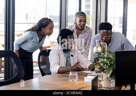 Diverse team collaborating enthusiastically around computer in modern office setting Stock Photo