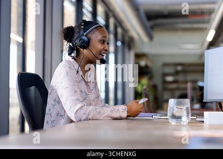 Smiling woman wearing headset working at office desk, engaging in conversation Stock Photo
