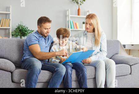Happy family sitting together on sofa with notebook, smiling parents helping their son with homework Stock Photo