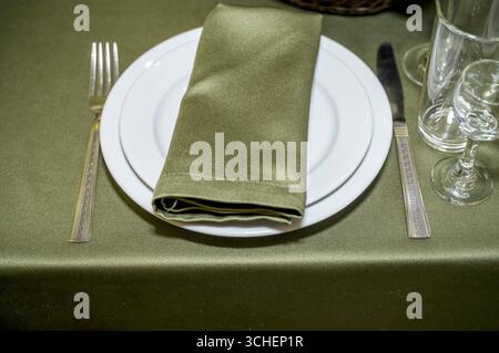 Festive table setting with white tableware. Empty plate and silver cutlery on dark green background.Dining table in a luxury restaurant. Festive table Stock Photo