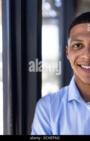 Smiling man in blue shirt standing by window at office, copy space Stock Photo