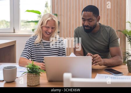 Young business couple, freelance workers, working at home office on laptop computer with tablet and graph statistics, economy and marketing experts, h Stock Photo