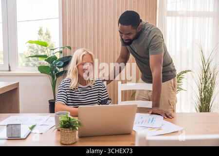 Young business couple, freelance workers, working at home office on laptop computer with tablet and graph statistics, economy and marketing experts, h Stock Photo