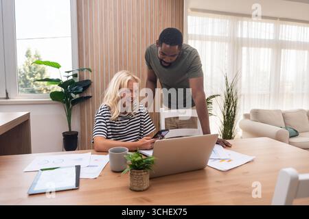 Young business couple, freelance workers, working at home office on laptop computer with tablet and graph statistics, economy and marketing experts, h Stock Photo
