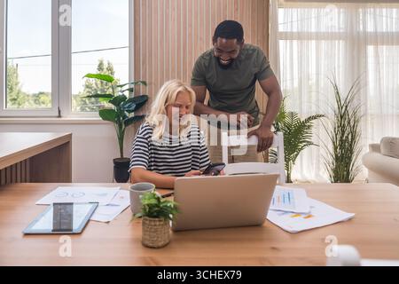 Young business couple, freelance workers, working at home office on laptop computer with tablet and graph statistics, economy and marketing experts, h Stock Photo