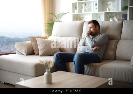 Sad man complaining alone looking through a window at home or hotel room Stock Photo