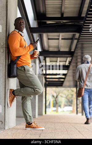African american man leaning on support column under metal roof with phone and coffee Stock Photo