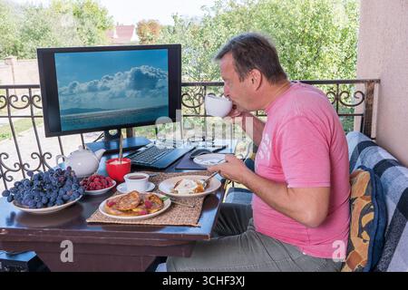 Man having breakfast on the balcony of his house near the computer. Close up Stock Photo