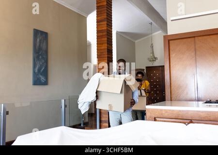 Happy couple carrying boxes while moving into new home, smiling with excitement Stock Photo