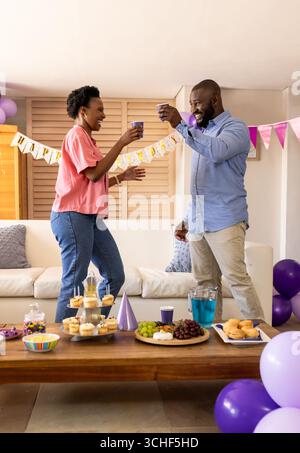 At party, Joyful couple celebrating at home, toasting with drinks during festive party Stock Photo