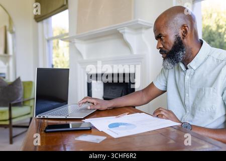 Working Senior African American man viewing pie chart on laptop at living room desk, copy space Stock Photo