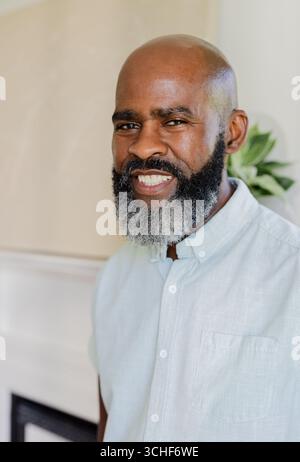 Smiling mature african american man wearing button-up shirt standing indoors with potted plant Stock Photo