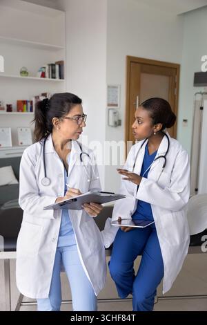 Two multiethnic, older and younger women physicians discussing patient case Stock Photo