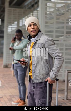 Diverse male travelers standing on transit platform checking wristwatch and holding smartphone Stock Photo