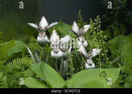 Unique metallic flowers emerge from vibrant greenery, creating a striking visual contrast in a tranquil garden environment. Stock Photo