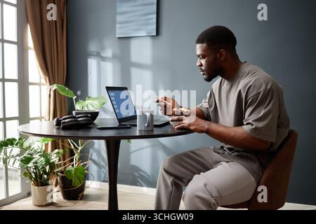 Adult Black Man Eating Breakfast While Working on Laptop during House Arrest Stock Photo