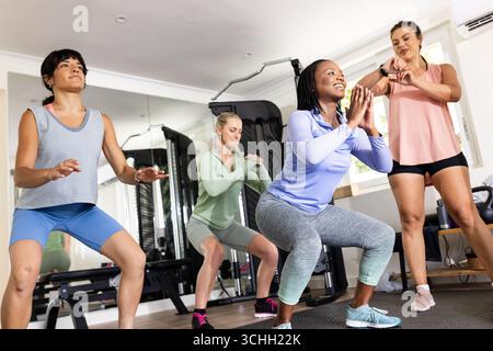 Diverse female friends exercising in gym, performing squats with focus and determination, at home Stock Photo