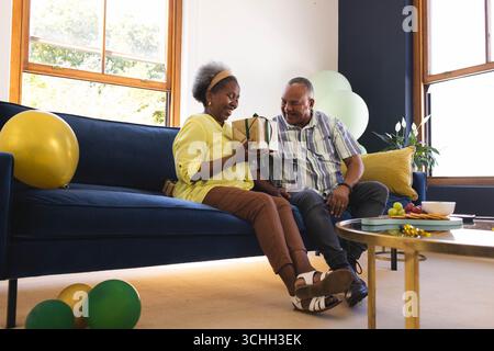 Celebrating birthday, senior couple sitting on sofa, exchanging gifts and joyful moments at home Stock Photo