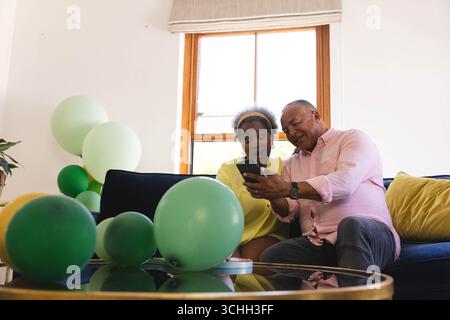 Celebrating birthday, Senior couple on sofa sharing joyful moment while looking at smartphone Stock Photo