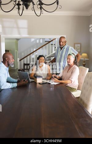Seniors discussing plans around table, using tablet and notebook at home Stock Photo