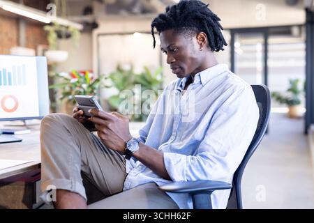 Focused professional using smartphone in modern office, analyzing data on screen Stock Photo