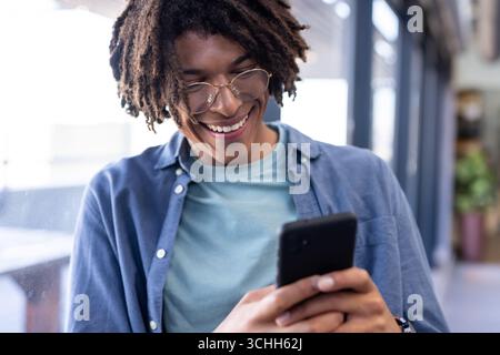In office, man using smartphone, reading positive message and smiling Stock Photo