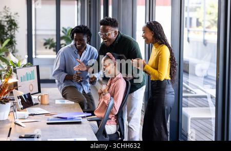 Diverse team celebrating success at office, gathered around computer with enthusiasm Stock Photo