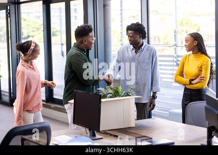 Diverse colleagues greeting each other with handshake in modern office, smiling and chatting Stock Photo