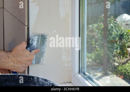 Caucasian plasterer man with a spatula applying finishing putty on a window opening Stock Photo