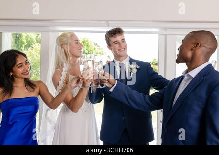Bride and groom toasting with friends, celebrating joyful wedding moment indoors Stock Photo