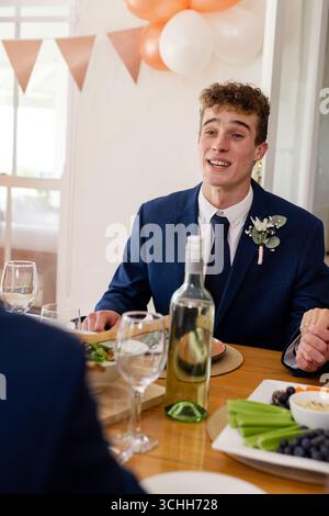Smiling man in suit enjoying wedding celebration meal with friends at table Stock Photo