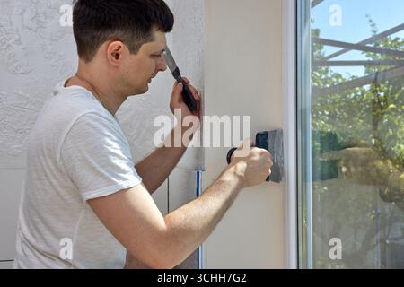 Caucasian plasterer man with a spatula applying finishing putty on a window opening Stock Photo