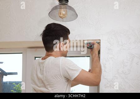 Caucasian plasterer man with a spatula applying finishing putty on a window opening Stock Photo