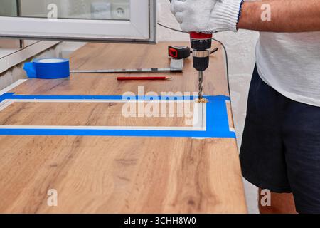repairman using electric drill for cutting hole for the sink in the kitchen countertops, installation new modern kitchen Stock Photo
