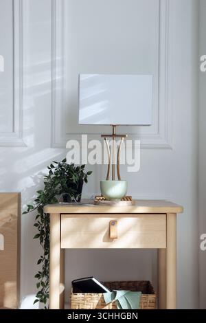 Bedside table with lamp and other decor near bed indoors Stock Photo