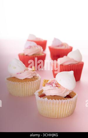 Six vanilla cupcakes with pink frosting, white meringue, and waffle cone pieces, arranged on a light pink surface in two neat rows. Stock Photo