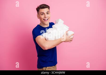 Cheerful young man holding a stack of white boxes with a smile on pink background, embodying joy and enthusiasm Stock Photo