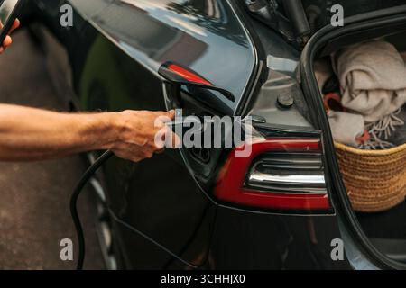 Hand of man plugging in electric plug for charging hybrid car Stock Photo