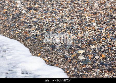 The tide of sea water with foam on the shore with small stony pebbles, close-up. Stock Photo
