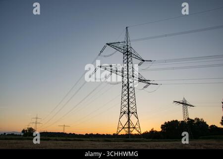 High-voltage electricity pylon photographed from below at blue hour shortly after sunset, silhouetted against the evening sky in Germany. Stock Photo