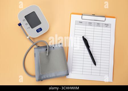 A blood pressure monitor with a data recording pad and pen is placed on the table, showing that it is a practice of self care by recording daily healt Stock Photo