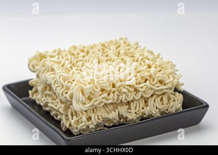 An uncooked instant noodle block on black plate raw ramen square dry wavy pasta beige color simple food minimal style studio light clean background co Stock Photo
