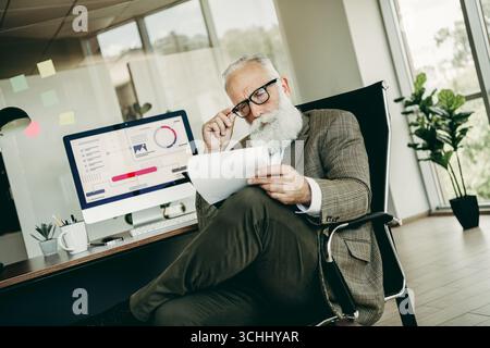 Mature businessman analyzing financial reports in a modern office, symbolizing professionalism, leadership, and corporate success Stock Photo