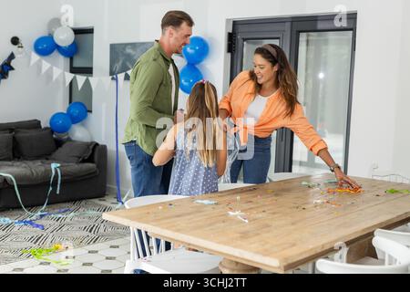 Family celebrating birthday at home, decorating table with balloons and confetti Stock Photo