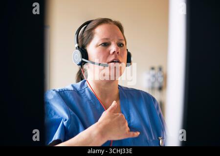 Female medical professional wearing headset gesturing while giving online consultation in clinic Stock Photo