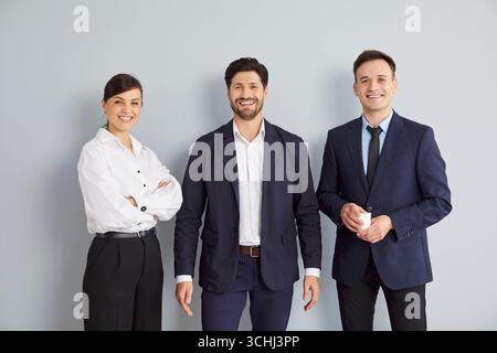 Three cheerful business people standing isolated on grey background and looking at camera. Stock Photo