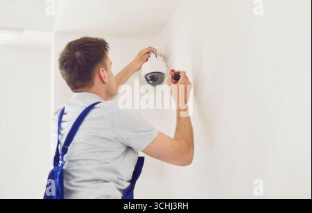 Portrait of young technician man installing surveillance CCTV camera on wall indoors. Stock Photo