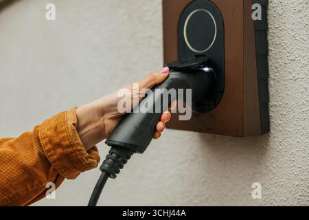 Close-up of woman plugging car charger in outlet mounted on wall Stock Photo