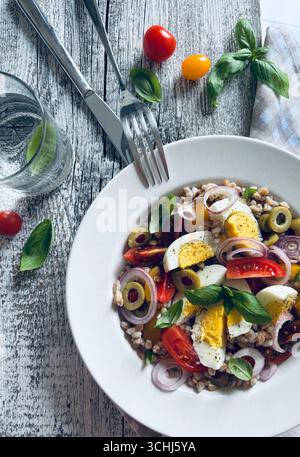 Homemade spelled salad with boiled eggs, fresh vegetables and basil on a wooden background. Spelt salad. Healthy food. Directly above. Stock Photo
